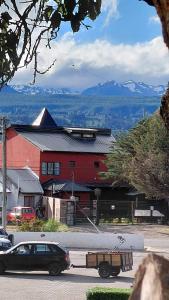 Un coche aparcado junto a un granero rojo con montañas al fondo. en ARWEN Suites 1, en Trevelín