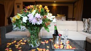 LUXURY EN-SUITE ROOM WITH LOUNGE @ 4 STAR GUEST HOUSE في ميدلبرغ: إناء من الزهور وزجاجة من النبيذ على طاولة