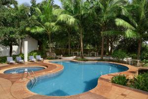 a swimming pool with chairs and palm trees at The Fern Samali Resort Dapoli, Series by Marriott in Dapoli