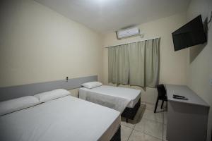 a room with two beds and a desk and a television at Vila Dumont no Centro de Foz in Foz do Iguaçu