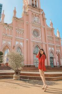 a woman standing in front of a pink building at MOONLIGHT Hotel & Suites - The Best City View, Dragon Bridge view in Da Nang