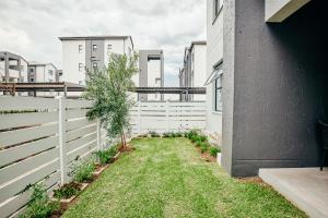 Stylish 1 Bed Garden Unit Power Backup في Sandton: سياج أبيض بجوار ساحة بها شجرة