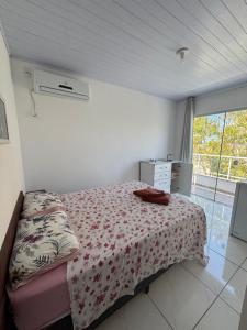a bedroom with a bed with a floral bedspread and a window at Residencial Dona Duda in Bombinhas