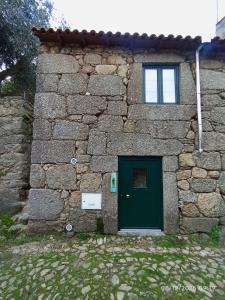 a stone building with a green door and a window at Casa de Aldeia Vale do Mondego in Guarda