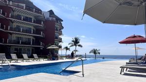 a hotel swimming pool with chairs and umbrellas and the ocean at VIVO Residences 2 Bedroom Ocean Front Condo 180 degree ocean views in Puerto Escondido +35 photos