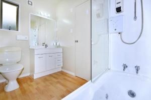 a white bathroom with a tub and a toilet at Anika Motel in Christchurch +9 photos