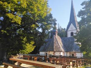 una iglesia con un campanario y bancos delante de él en Koča na Pikovem, en Črna na Koroškem