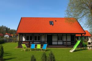 an orange roofed house with chairs and a playground at Kaszëbsko Nórcëk 8-10 osób 4 sypialnie jezioro las park linowy łowisko wędkarskie in Załakowo