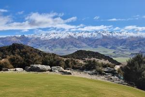 a green field with snow covered mountains in the background at Bendigo Ridge - Where Activity is Relaxing in Cromwell