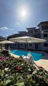 a swimming pool with two chairs and an umbrella at Merepe Residence in Porto De Galinhas