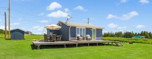 une petite maison bleue avec des chaises et un parasol dans l'établissement PEI Ocean Front Beach House, à OʼLeary