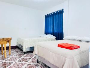 two beds in a room with blue curtains and a table at Hotel Julián Cotuc in San Juan La Laguna