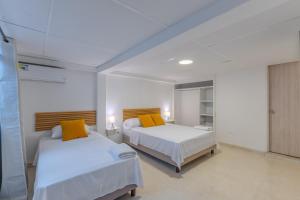 two beds in a room with white walls and yellow pillows at Hotel Stadio Cali in Cali