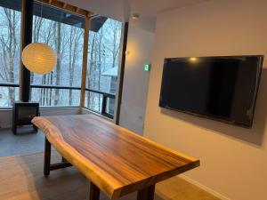 The Guest House Japan Hakuba في هاكوبا: غرفة معيشة مع طاولة خشبية وتلفزيون بشاشة مسطحة