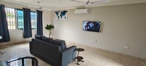 a living room with a couch and a tv on the wall at Purple Springs Elmina #1 in Esamang +3 photos