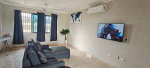 a living room with a couch and a tv on the wall at Purple Springs Elmina #1 in Esamang