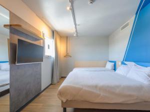 Un dormitorio con una cama y un televisor. en Ibis Budget La Rochelle Puilboreau, en Puilboreau