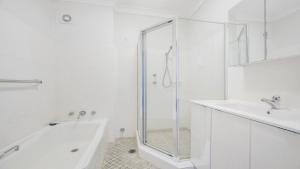 a white bathroom with a shower and a tub and a sink at Flynns Beach Seascape in Port Macquarie +9 photos