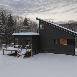 a black house with a deck in the snow at Le Belvédère - Retraite scandivane in Saint Adolphe D'Howard