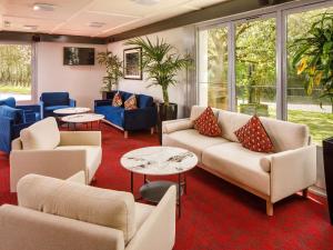 Una sala de espera con sofás, mesas y ventanas. en ibis Coventry South, en Coventry