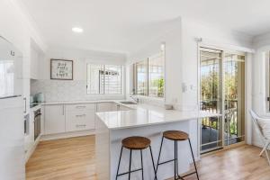 a kitchen with white cabinets and a counter with stools at Spades - at Lighthouse Beach in Port Macquarie +7 photos