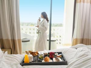 a woman in a robe with a tray of food on a bed at Sofitel Rabat Jardin Des Roses in Rabat +167 photos