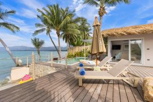 a deck with chairs and an umbrella and the ocean at Little Me Beachfront Villa in Nathon Bay
