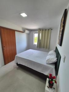 een slaapkamer met een bed met witte lakens en een raam bij Condomínio Residencial Tiê in Camassari