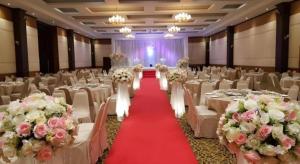 Western Grand Hotel Ratchaburi في راتشابوري: قاعة احتفالات مع كراسي بيضاء وطاولات بها ورد