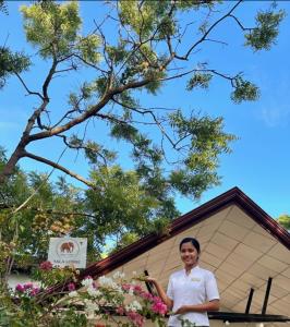Neem safari lodge Yala في تيساماهاراما: امرأة تقف أمام مبنى به زهور