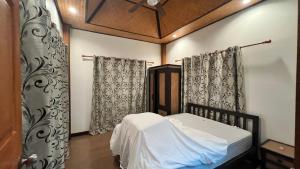 a small bedroom with a bed and curtains at บ้านกูรูรีสอร์ท in Ban Thung Satong