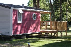 une petite maison rose avec une terrasse couverte en bois dans l'établissement Camping Fleur d'Oleron, à Saint-Pierre-dʼOléron