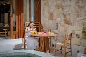 a woman sitting at a table near a pool at Casa Beso Balangan in Badung