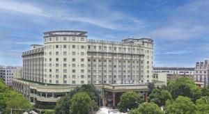 New Century Hotel Taizhou في Daidong: مبنى ابيض كبير في مدينة بها اشجار