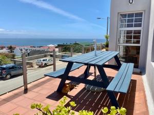 a blue picnic table and a cat sitting on a patio at Sunrise & Sunset Haven in Mossel Bay