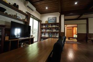 おこさま連れ限定一棟貸し的場邸 : شخص يجلس على طاولة خشبية كبيرة في غرفة بها تلفزيون