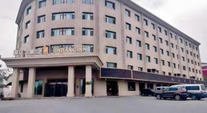 Jinjiang Inn Select Urumqi Midong Avenue في Miquan: مبنى كبير مع سيارات متوقفة أمامه