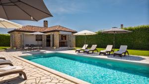 a pool with chairs and umbrellas next to a house at Rustic villa Inga with pool and grill in Buje in Kaštel