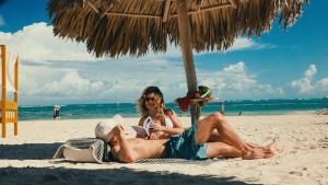 a man and woman laying on the beach under an umbrella at Zel Punta Cana - All Suites in Punta Cana