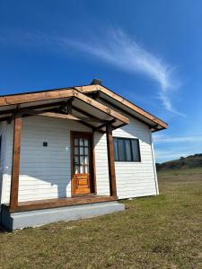 een klein wit huis met een houten deur bij Cabana Jardim das Nuvens in Urupema