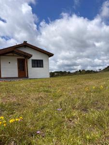 een klein wit huis in een veld met bloemen bij Cabana Jardim das Nuvens in Urupema