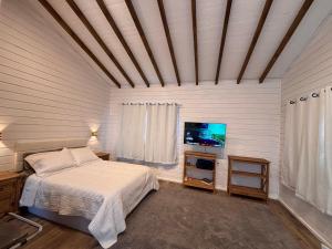 een slaapkamer met een bed en een flatscreen-tv bij Cabana Jardim das Nuvens in Urupema