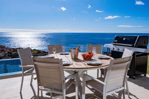 a table with chairs and a grill on a balcony with the ocean at Villa Infinityviews Madeira in Câmara de Lobos