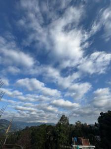 een blauwe, bewolkte lucht met bomen op de achtergrond bij Green Hill Home in Mirik