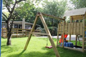a wooden swing set in a yard with a tree at glamping luxe caravan in Oosterend