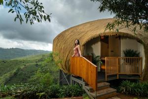 uma mulher em pé na varanda de uma casa de palha em Monticle Glamps em Vagamon