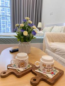 twee koffiekopjes en een vaas met bloemen op een tafel bij Lily House in Kon Rung (1)