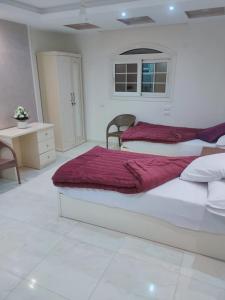 a white bedroom with two beds and a desk at رويال للغرف الفندقية in Mît Khamîs