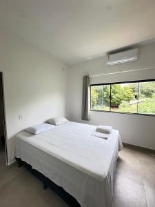 a white bedroom with a large bed and a window at Pousada caminho das águas in Pirenópolis