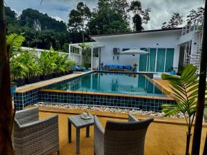 a swimming pool with chairs and a table in front of a house at Beautiful villa between jungle in Ban Chong Phli
